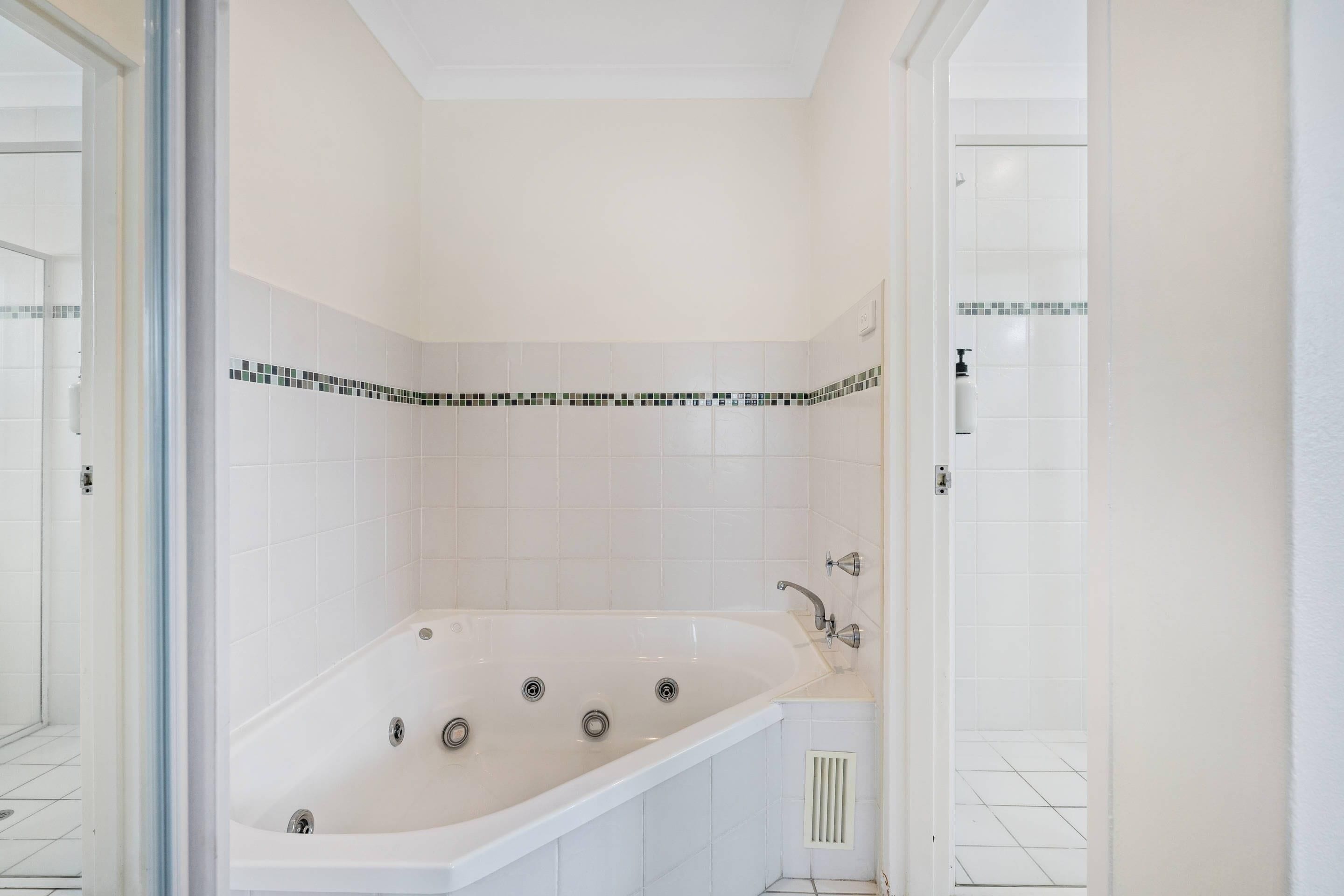 A bathroom with a white bathtub, white tiled walls, and a white floor.