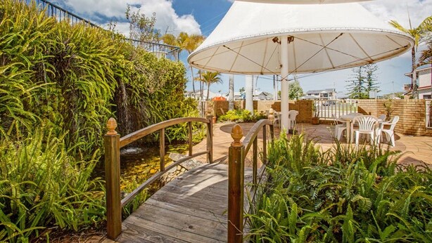 A wooden deck with a bridge, surrounded by lush greenery and a white umbrella structure.