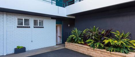 A multi-level building with white brick walls, a dark facade, and a small garden area with plants.