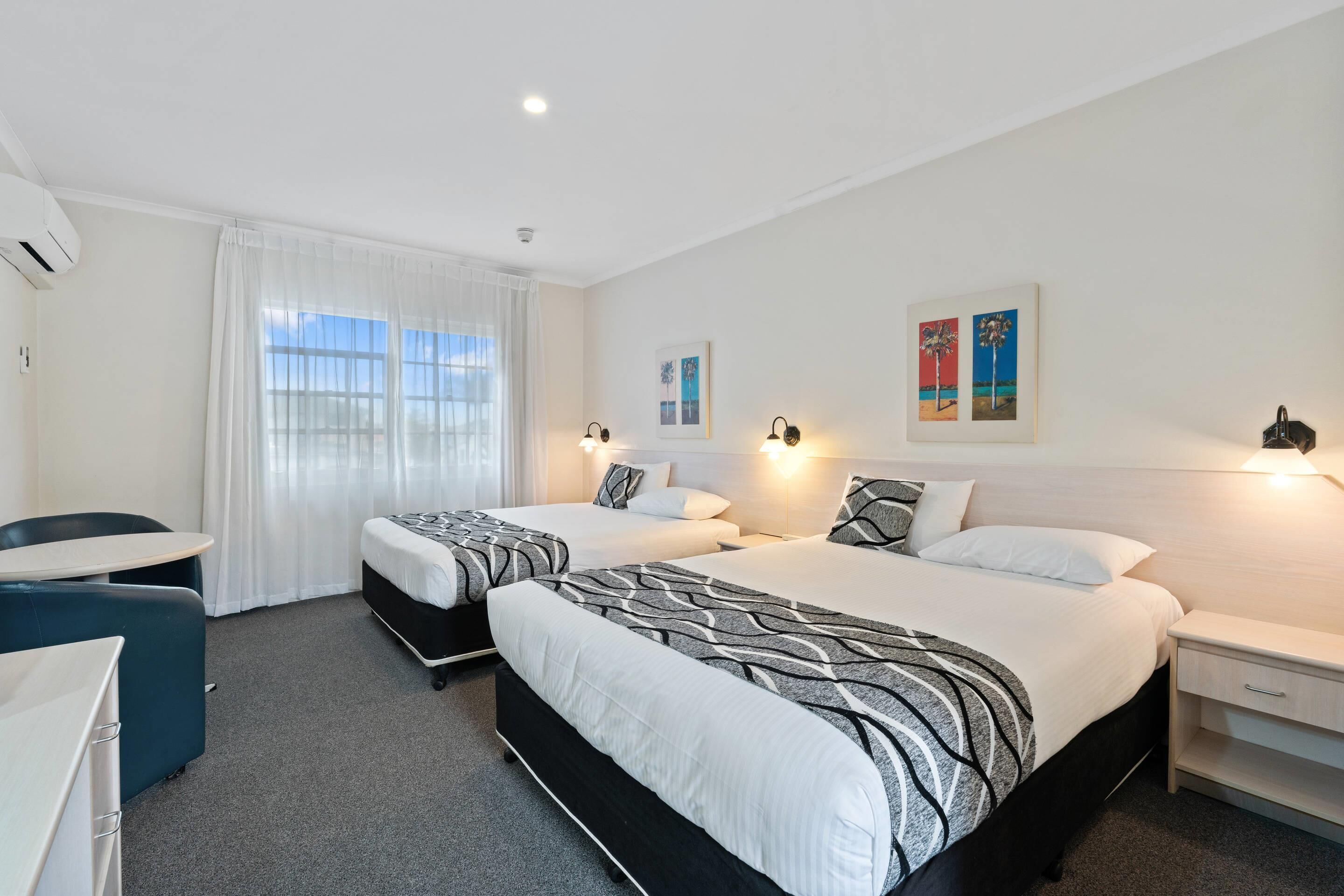 A hotel room with two beds, a desk, and a chair.