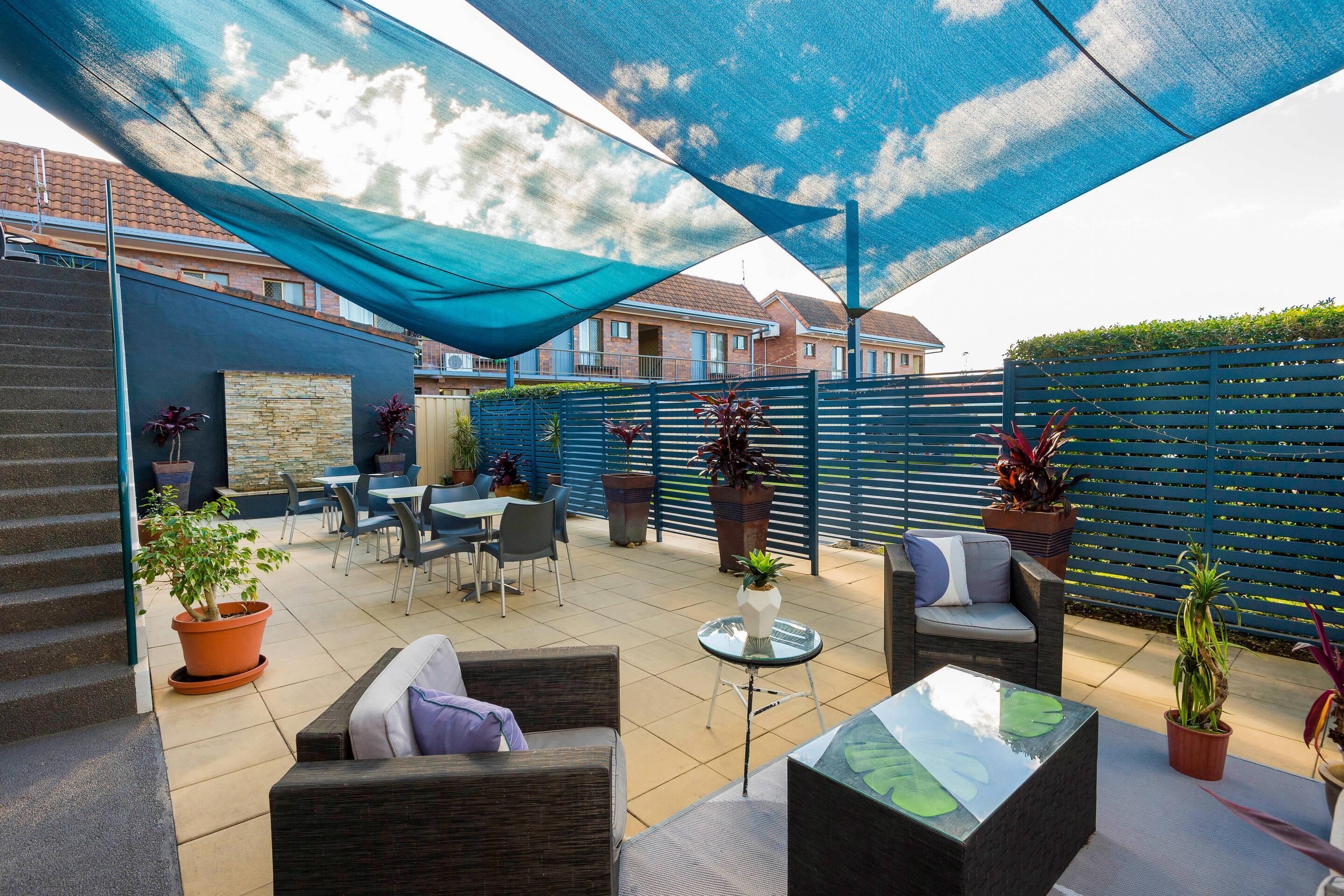 An outdoor patio area with outdoor furniture, potted plants, and a blue shade sail.