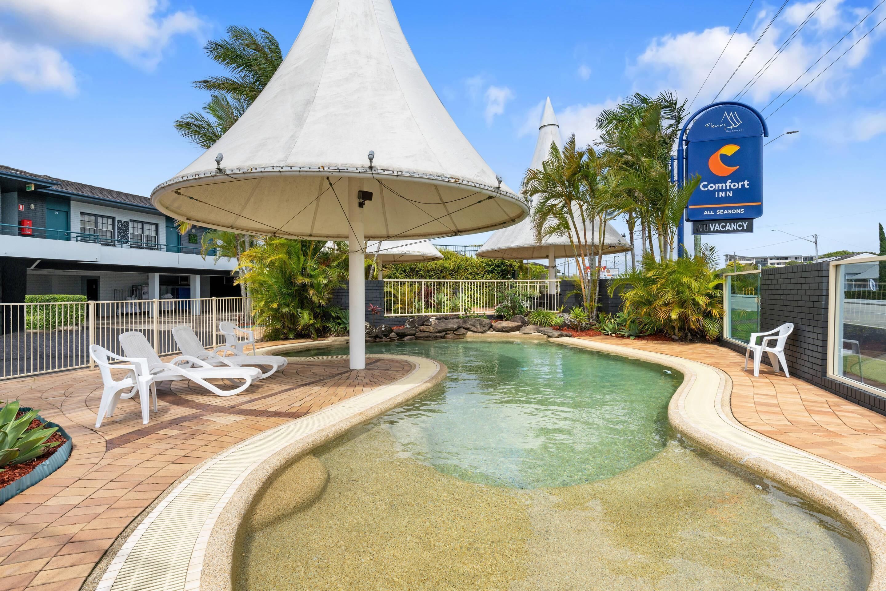 A hotel pool area with lounge chairs, umbrellas, and a sign for the Comfort Inn.