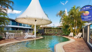 A pool area with lounge chairs, a covered seating area, and a Comfort Inn sign.