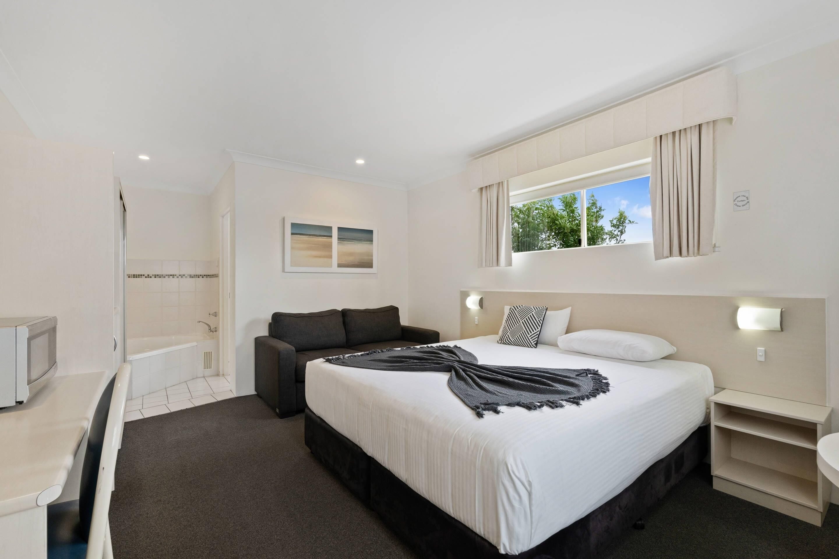 A hotel room with a bed, a sofa, a small table, and a window with curtains.