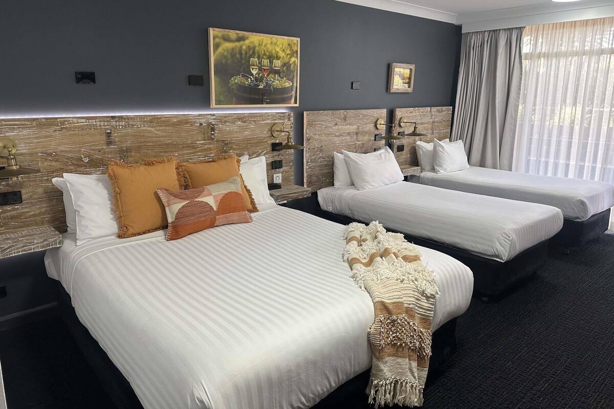 A hotel room with two beds, a headboard with a rustic design, a framed picture on the wall, and a window with curtains.