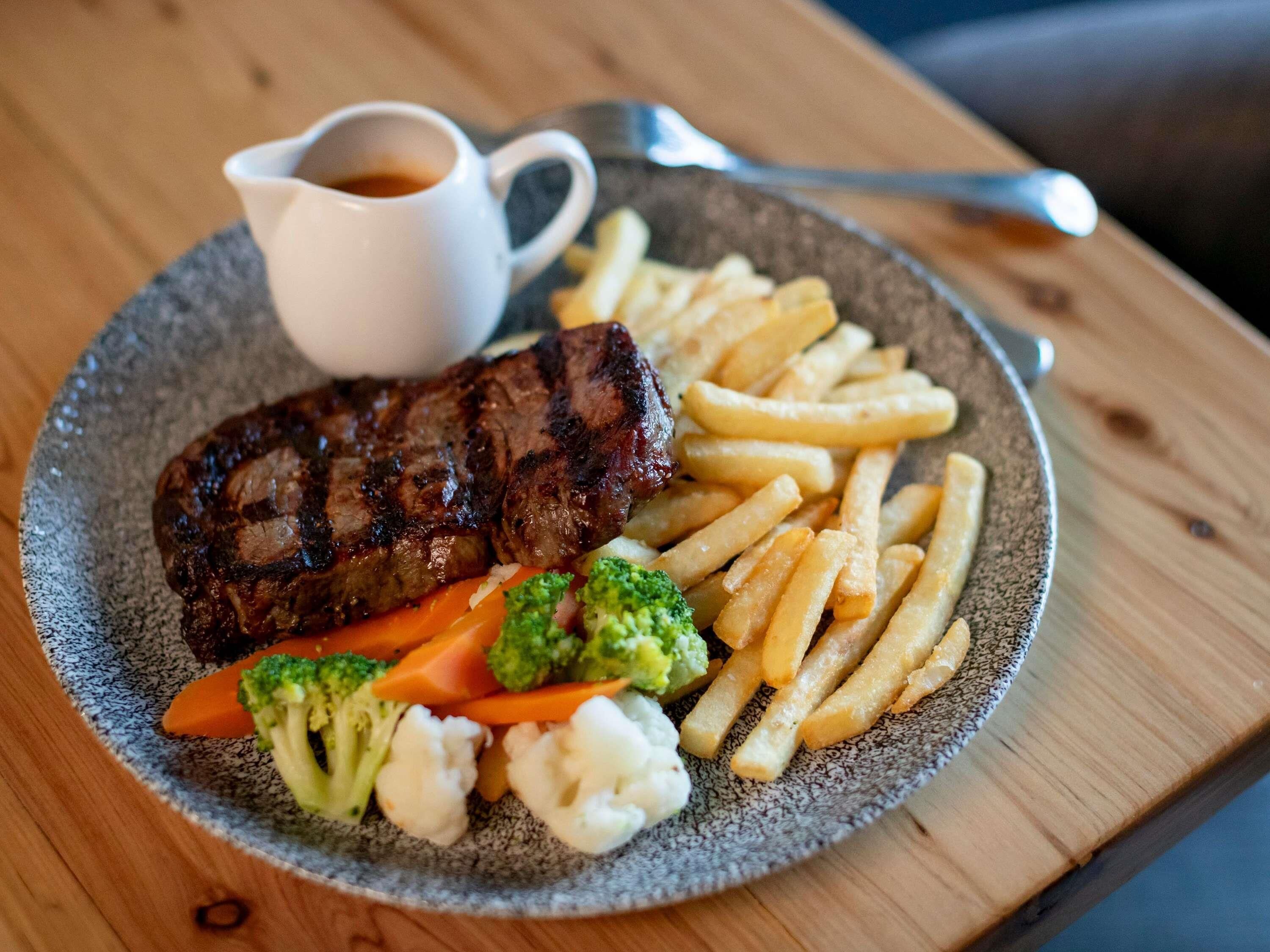Un plato con bistec, papas fritas y verduras sobre un plato con motas.