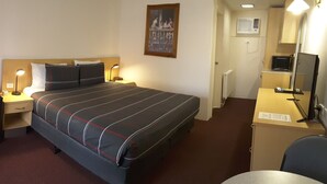 Quarto de hotel com cama, escrivaninha, cadeira, luminária e espelho.