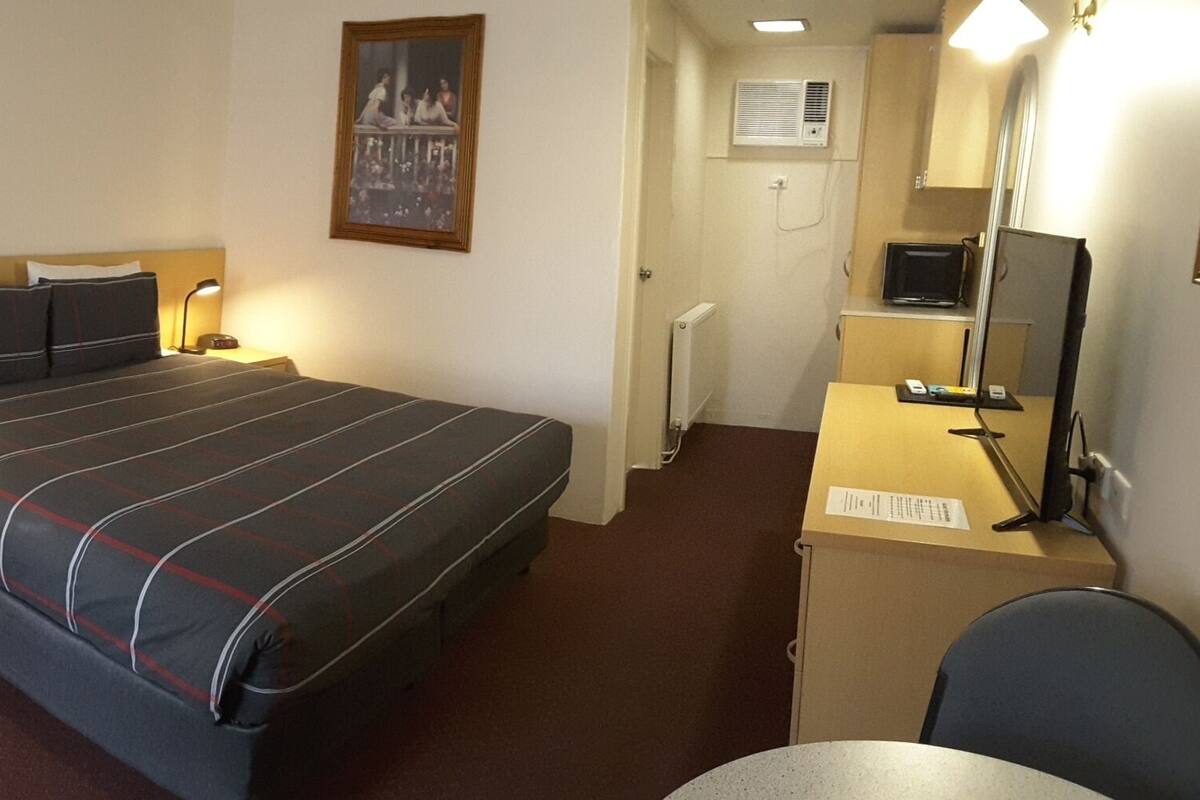 A hotel room with a bed, a desk, a chair, a lamp, and a mirror.