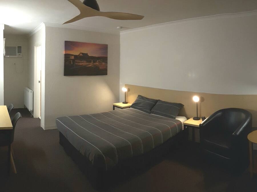 Een hotelkamer met een bed, een bureau, een stoel, een lamp en een plafondventilator.