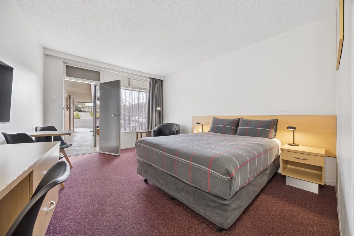 Ein Hotelzimmer mit Bett, Schreibtisch, Stühlen und Blick durch eine Tür.