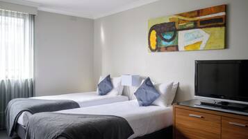 A hotel room with two beds, a flat-screen TV, a wooden dresser, and a painting on the wall.