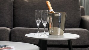 A modern living room with a grey sofa, a small round table with a book, two glasses, and a champagne bottle in a metal bucket. - Crest on Barkly (St Kilda)