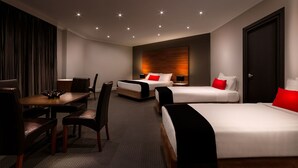 A hotel room with two beds, a dining table, chairs, and a wooden accent wall. - Crest on Barkly (St Kilda)