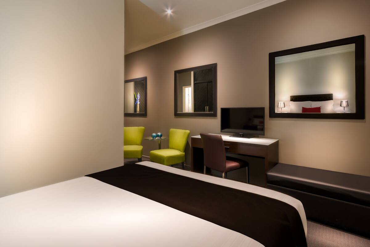 A hotel room with a bed, a desk, two chairs, a television, and a large mirror.