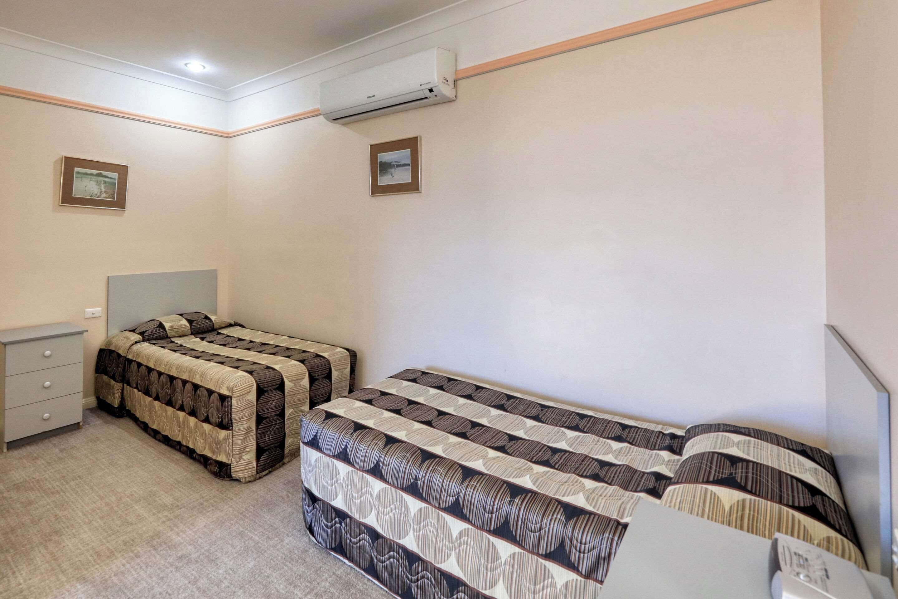 Un dormitorio con dos camas, un aparador y un equipo de aire acondicionado.