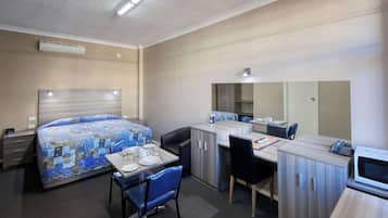A hotel room with a bed, a desk with a chair, a microwave, and a small kitchenette.