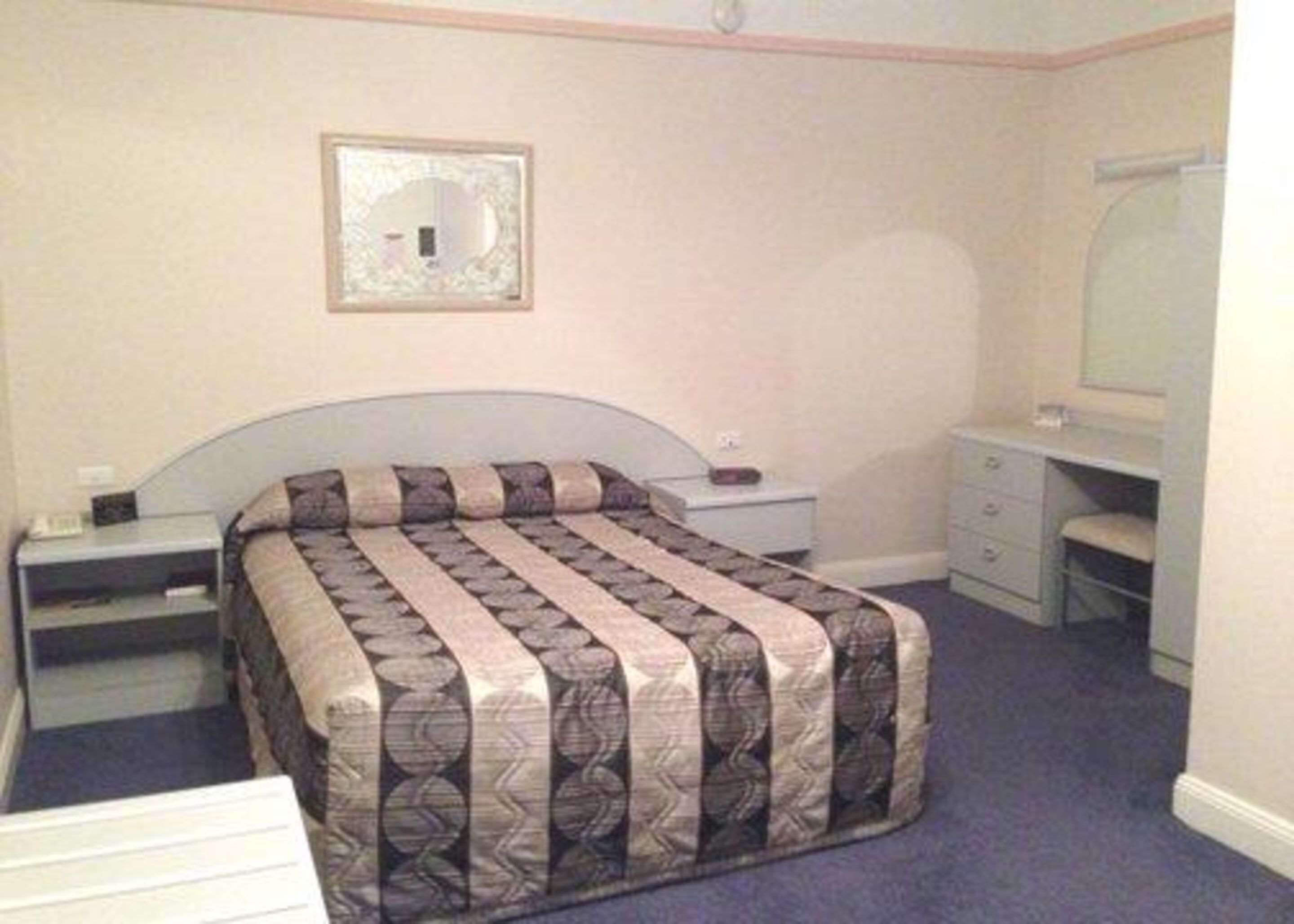 A bedroom with a bed, a nightstand, a dresser, a mirror, and a wall-mounted picture.