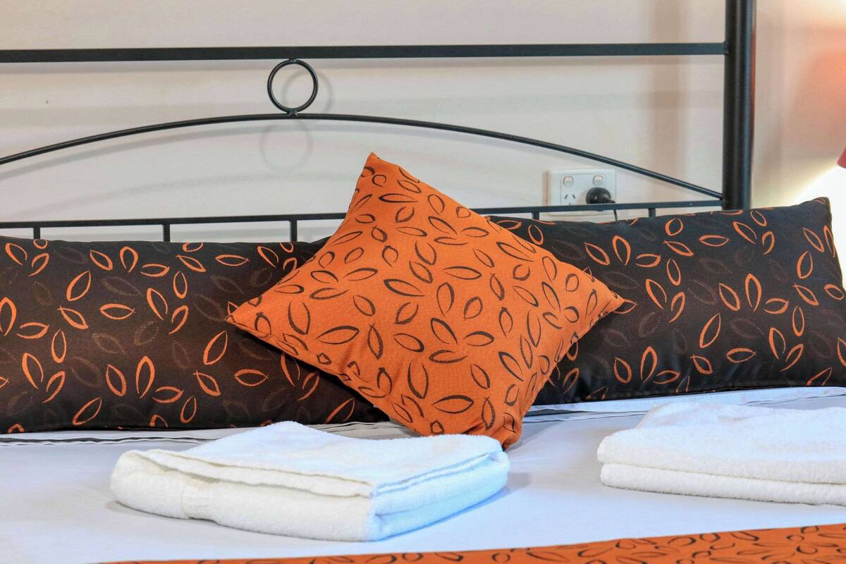 A neatly made bed with patterned pillows and folded towels.