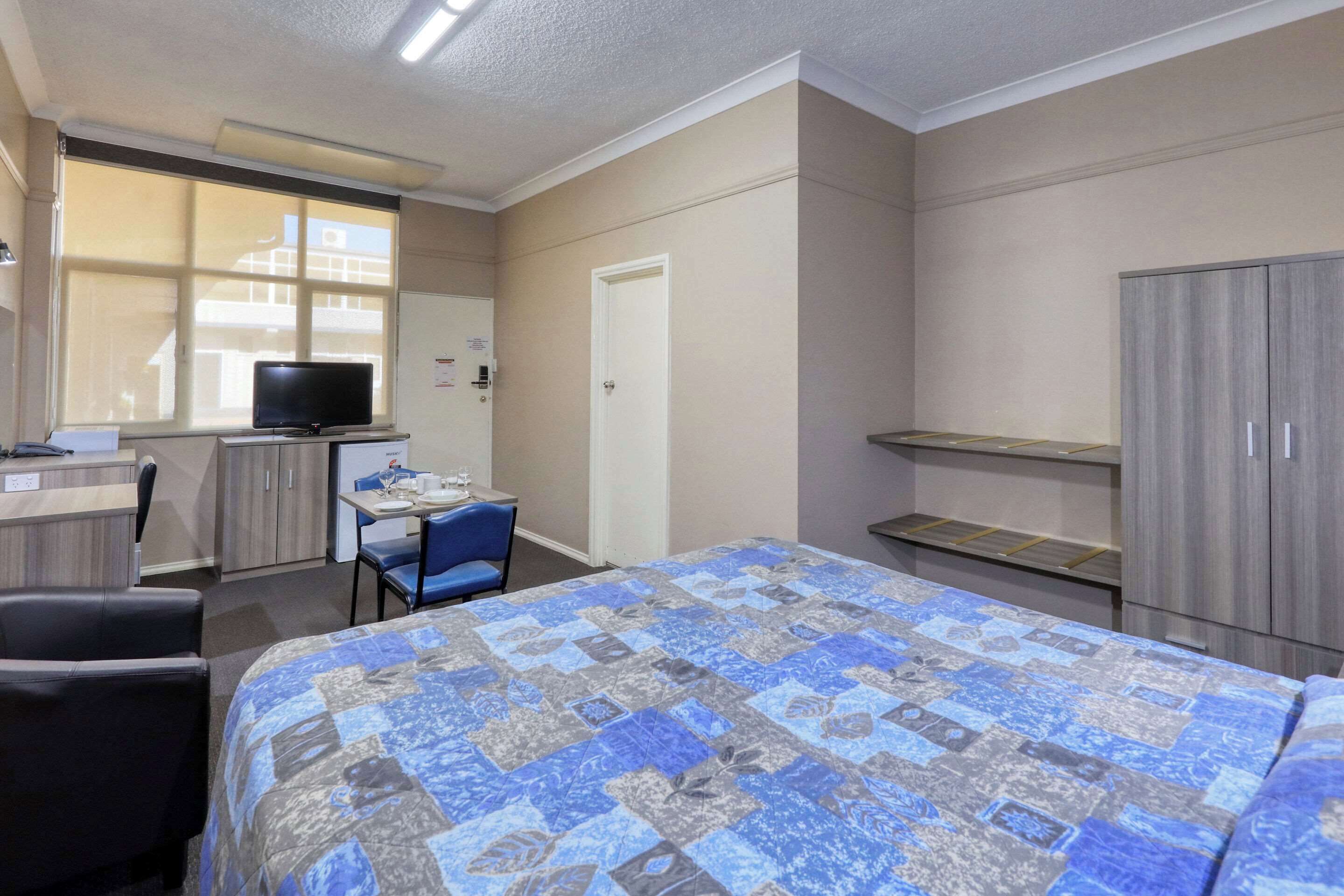 Une chambre d’hôtel comprenant un lit, un bureau avec un ordinateur, une chaise, une télévision et une armoire.
