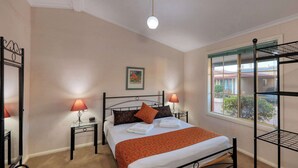 Une chambre à coucher bien rangée, avec un lit, deux tables de chevet, une fenêtre donnant sur un beau paysage et une étagère en métal.