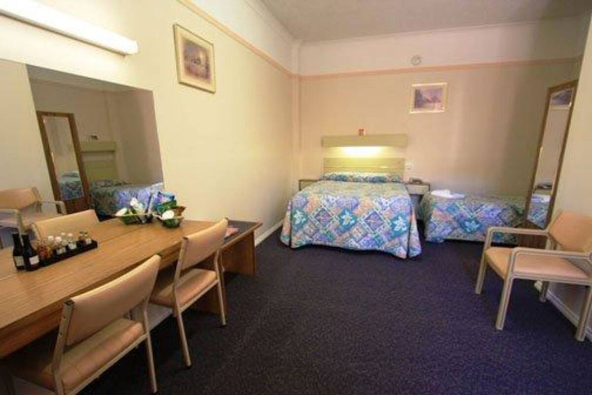 A hotel room with a bed, a desk, a chair, and a dresser.