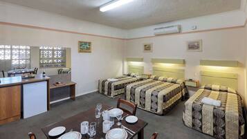 Habitación de hotel compacta con kitchenette, dos camas con cabeceros, una mesa de comedor para cuatro personas y una pequeña zona de estar.