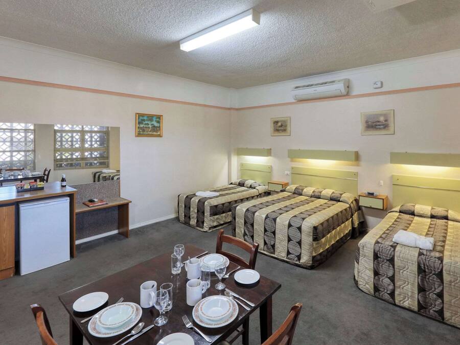 Habitación de hotel compacta con kitchenette, dos camas con cabeceros, una mesa de comedor para cuatro personas y una pequeña zona de estar.