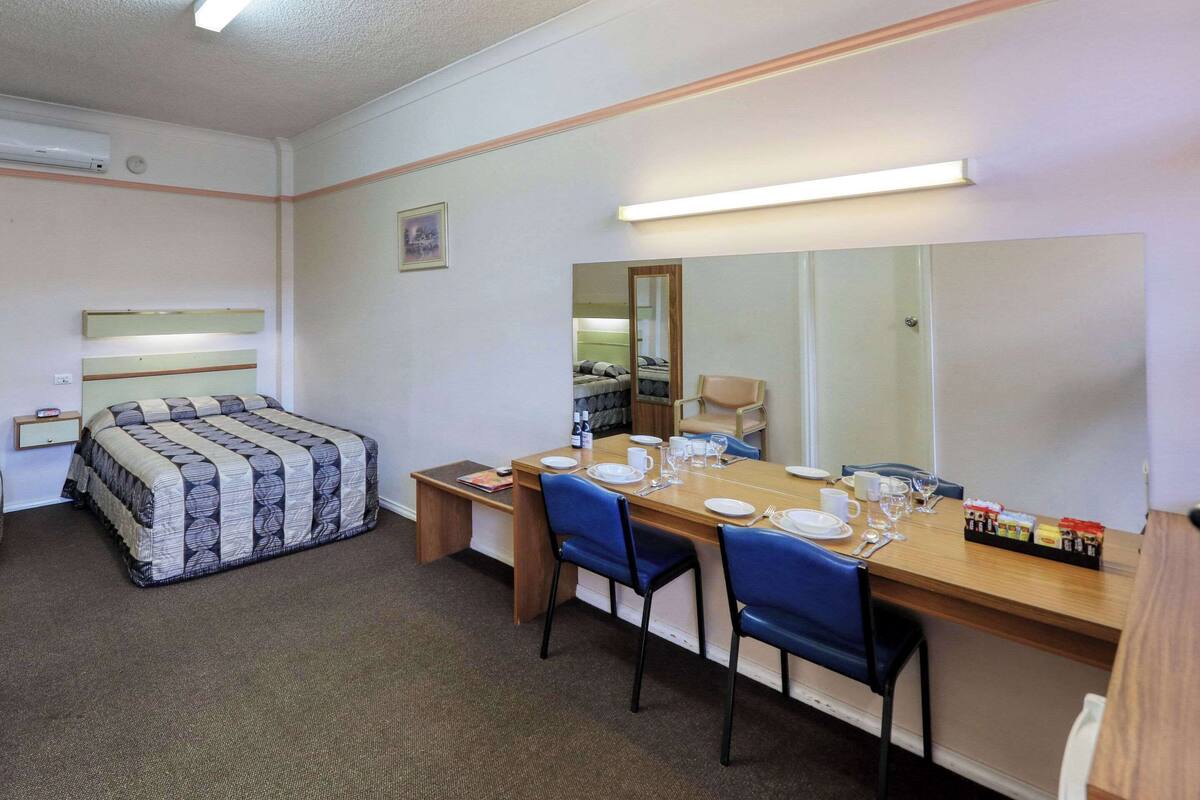 A hotel room with a bed, a desk with chairs, a dining table set for two, and a large mirror.