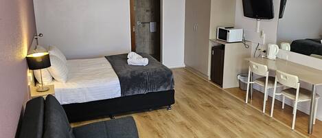 Una habitación de hotel moderna con una cama, un sofá, un escritorio, un televisor y un microondas.