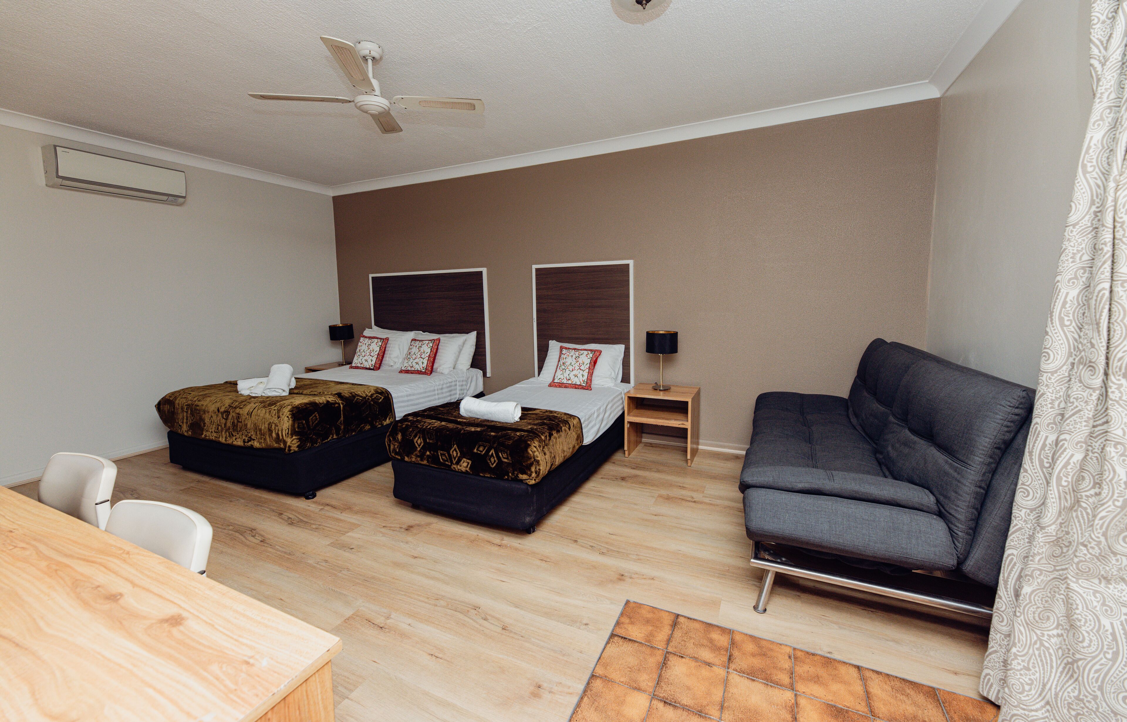 Habitación de hotel con dos camas, un sofá, un escritorio y un ventilador de techo.