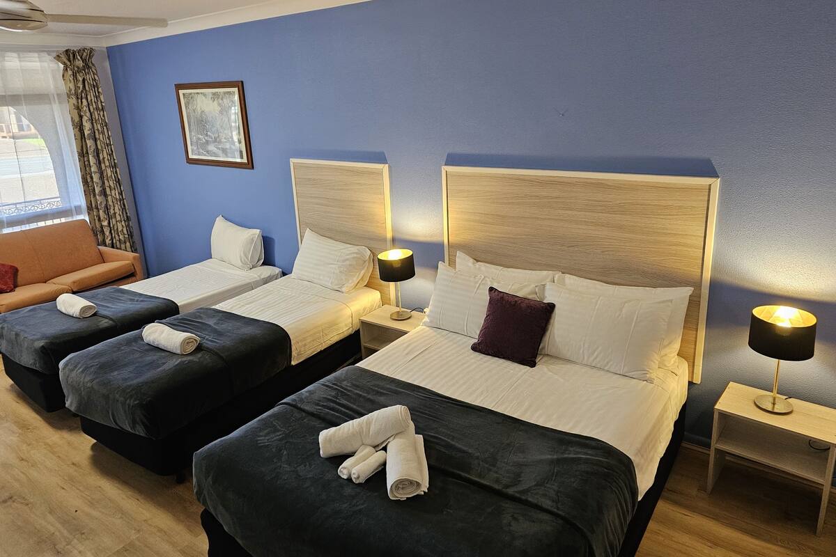 A hotel room with two beds, a sofa, and a ceiling fan.