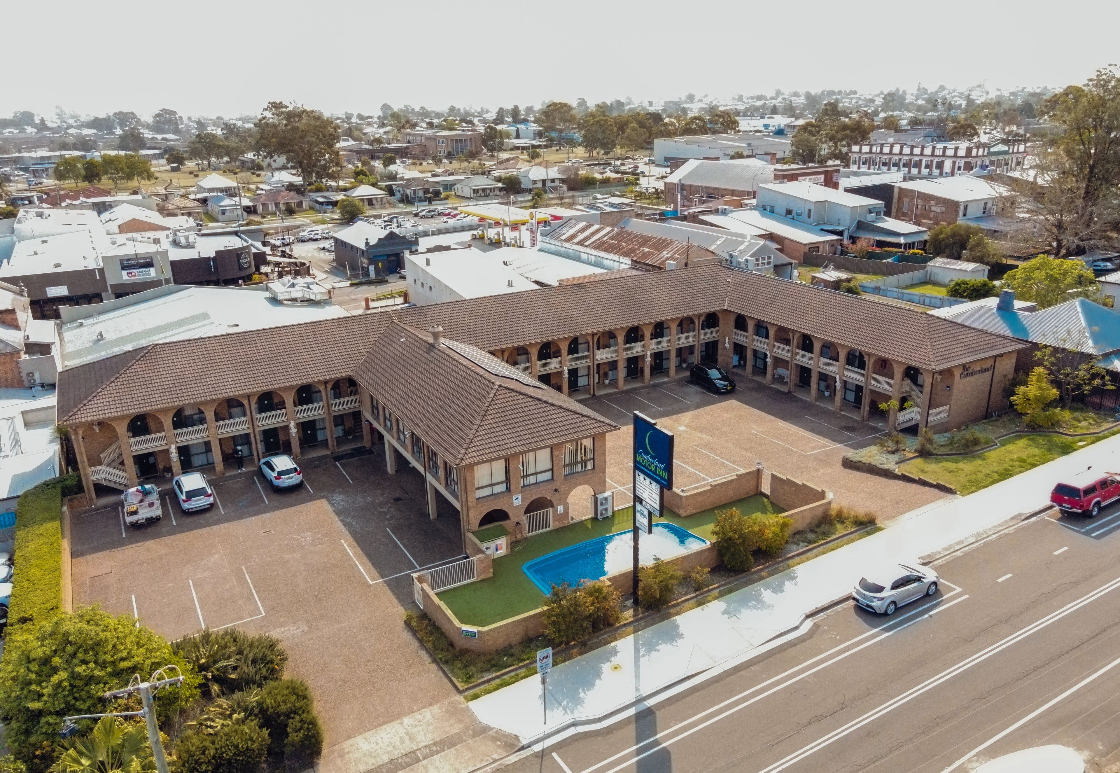 A multi-story hotel with a central courtyard, parking lot, and swimming pool.
