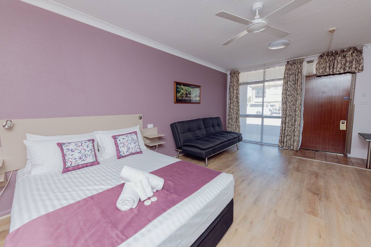 A hotel room with a bed, a sofa, a ceiling fan, and a door with curtains.