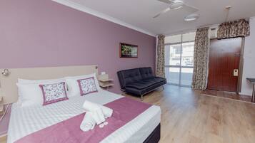 Una habitación de hotel con cama, sofá, ventilador de techo y una puerta con cortinas.