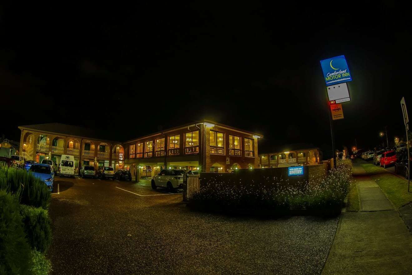 A motel with a large building, multiple parking spaces, and a signboard.