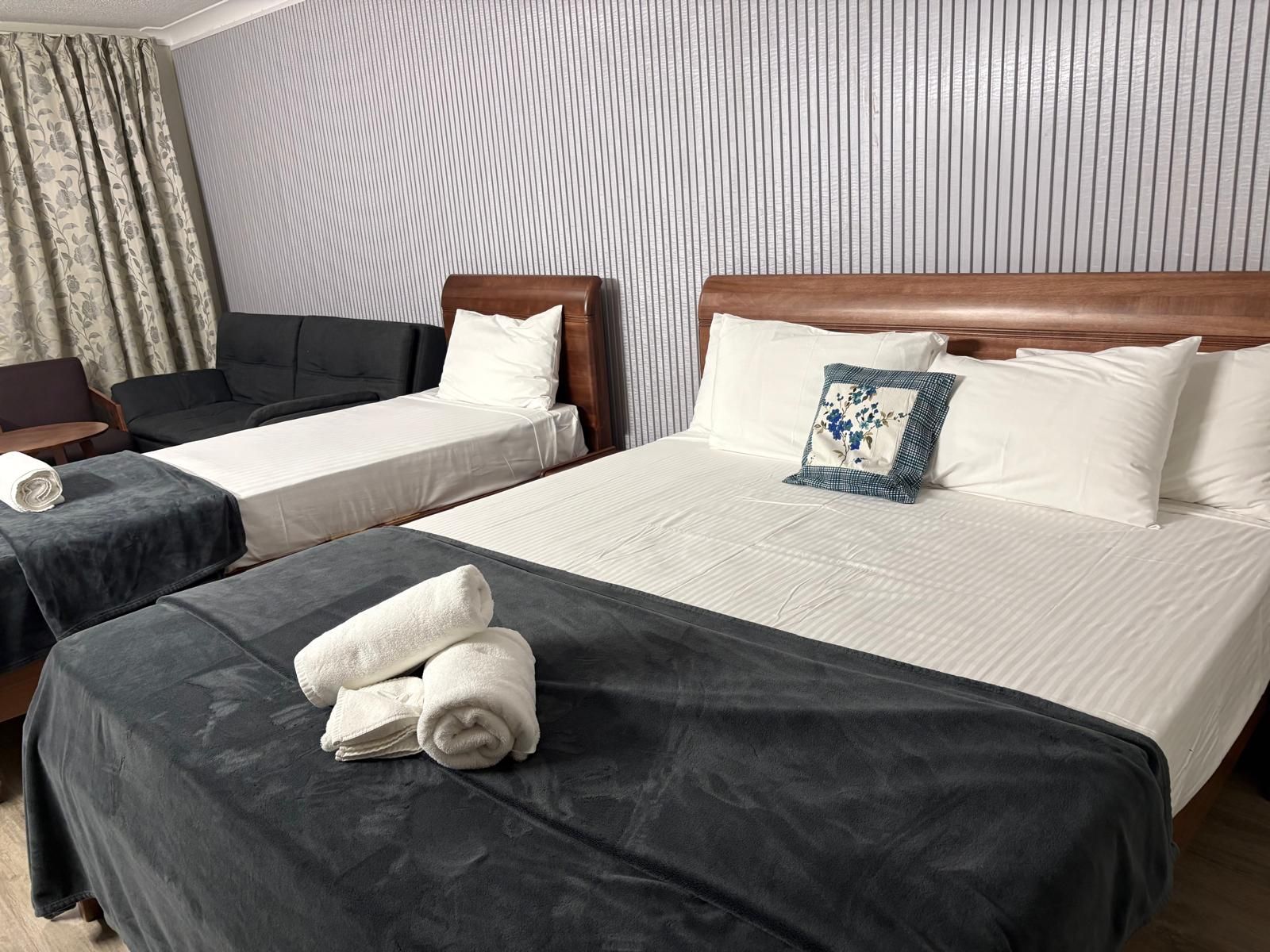 A hotel room with two single beds, a sofa, and a chair.