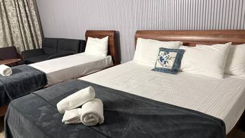 A hotel room with two single beds, a sofa, and a chair.