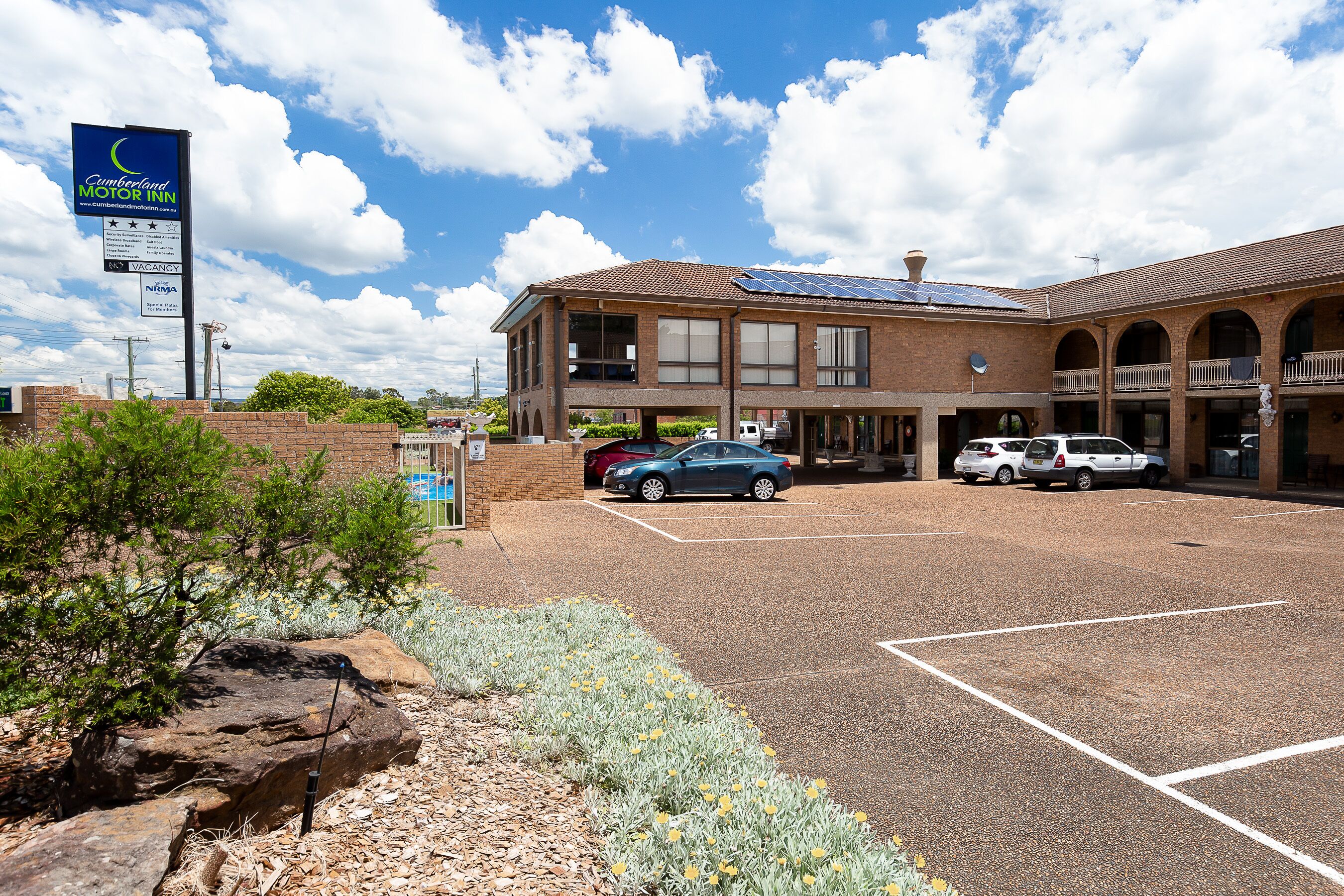 A motel with a parking lot, a signboard, and a building with a brick facade and solar panels.