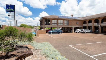 A motel with a parking lot, a signboard, and a building with a brick facade and solar panels.