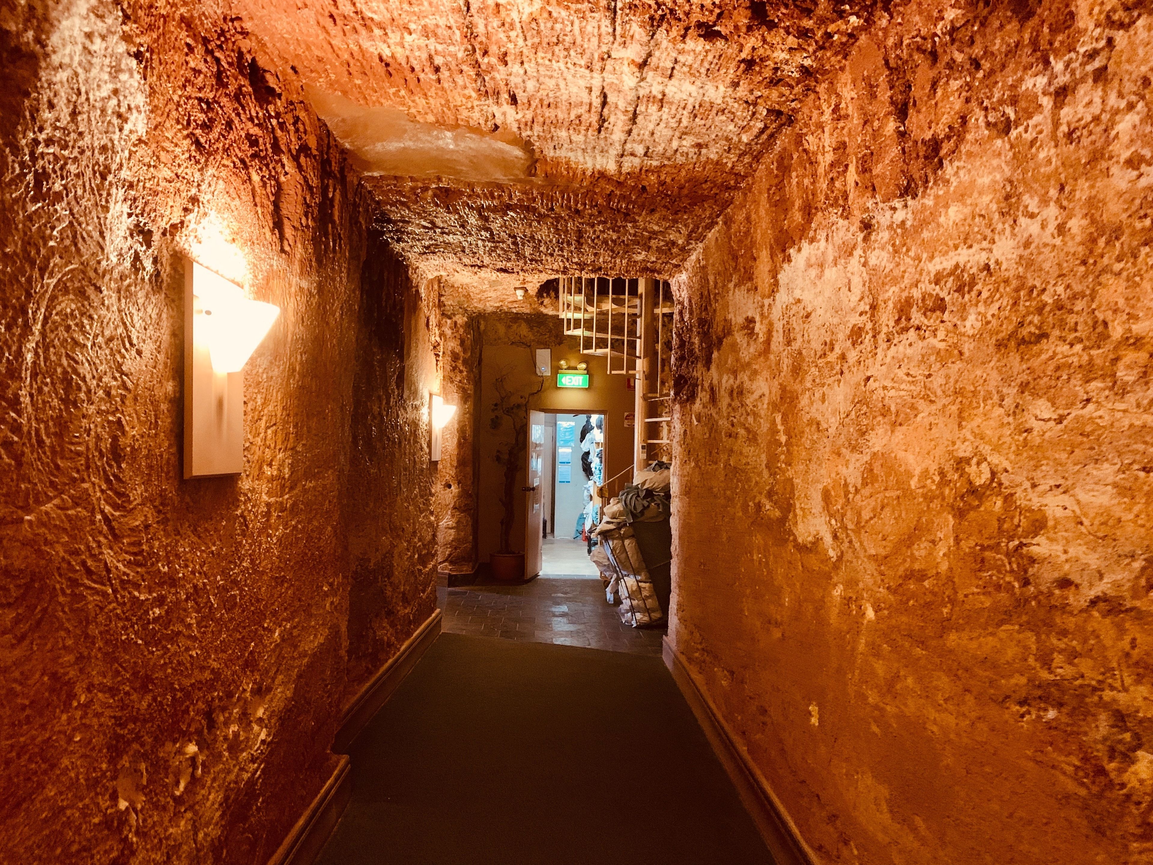 Un couloir étroit et faiblement éclairé, aux murs rugueux et texturés, et dont le sol est recouvert de carreaux.