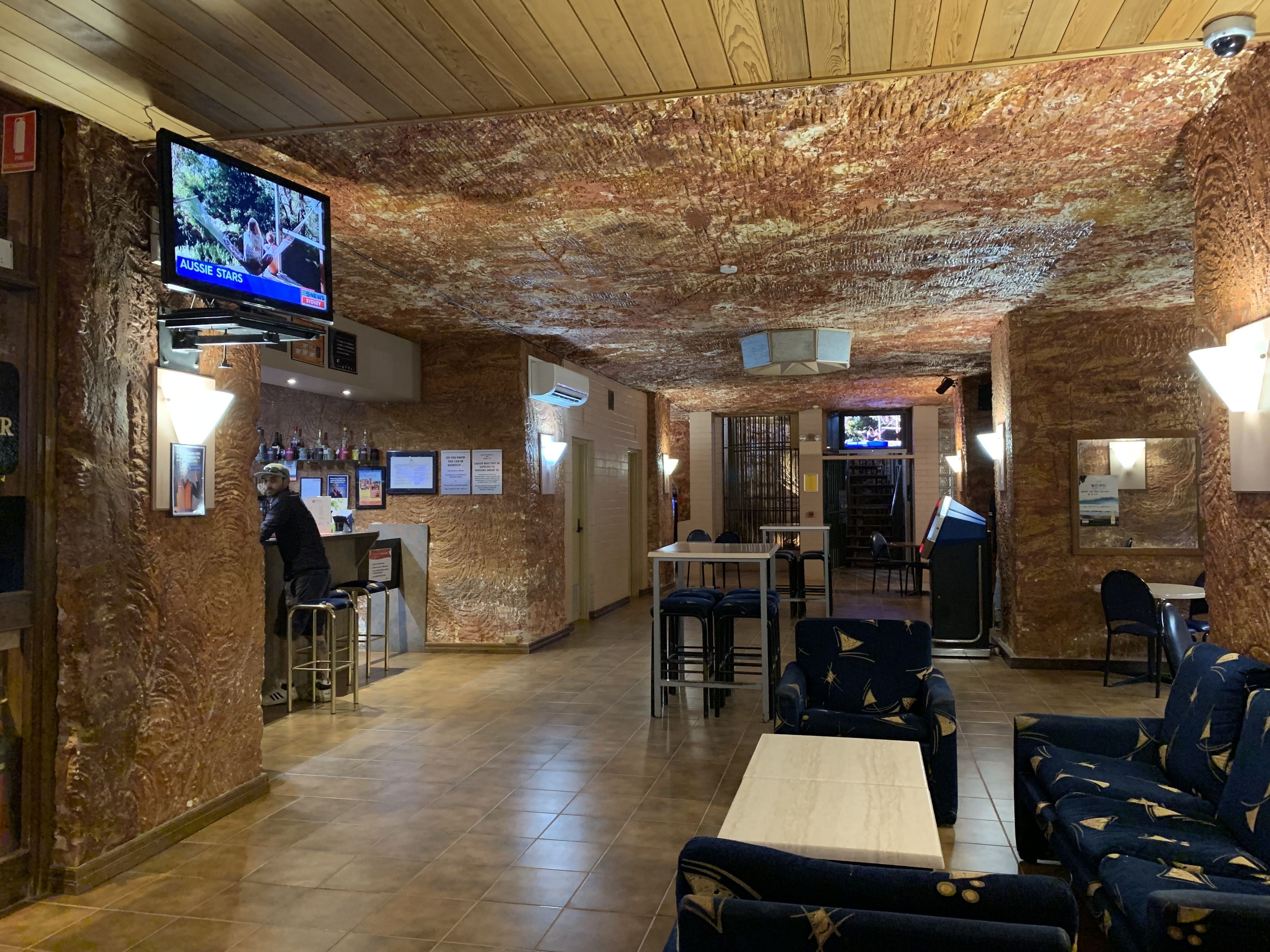 A restaurant with a rustic interior, featuring a wooden ceiling and walls, a bar area, and seating arrangements.