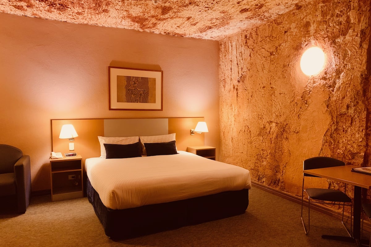 A hotel room with a large bed, two bedside tables with lamps, a chair, and a table.