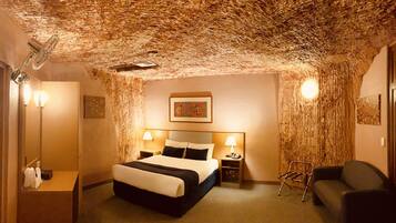 A hotel room with a unique textured ceiling, a bed with a black and white bedspread, two bedside lamps, a nightstand with a phone, a chair, and a small table with a lamp.