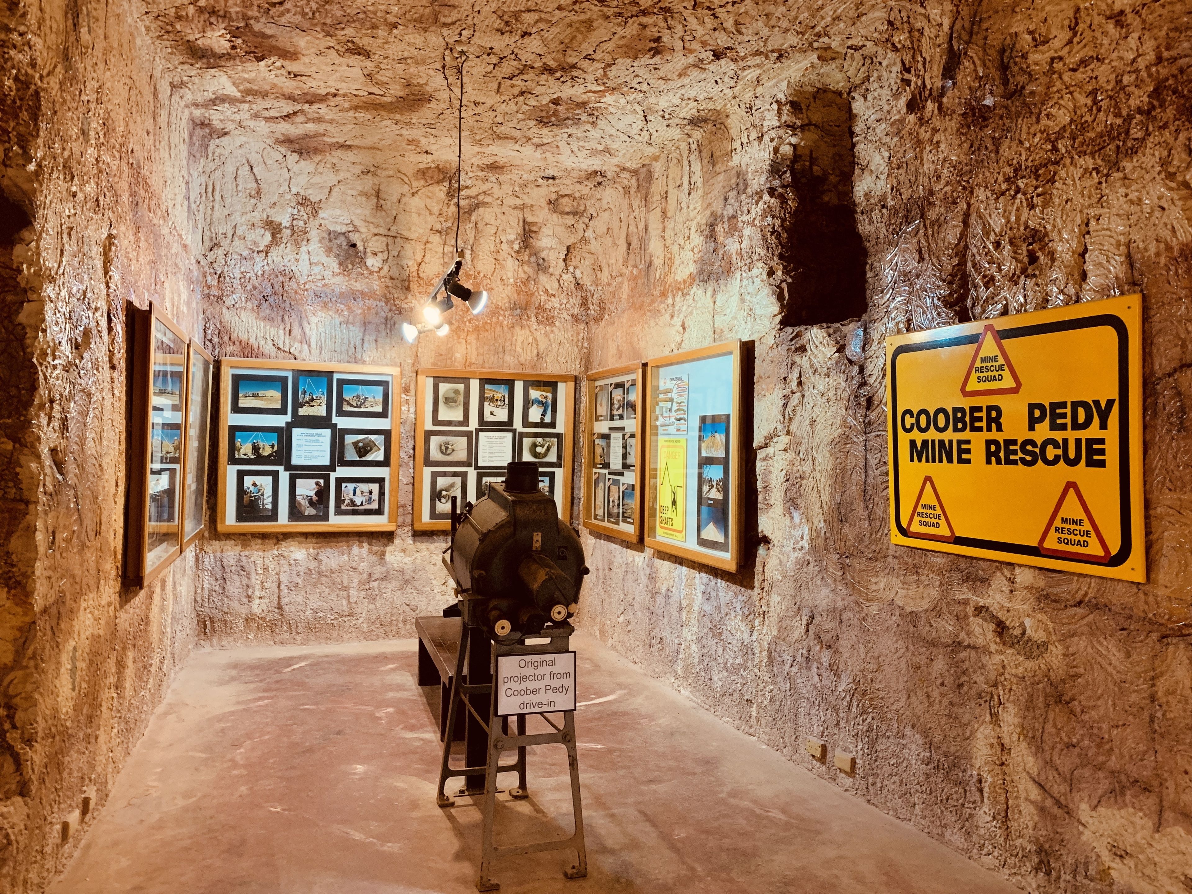 An underground mine with framed pictures on the walls and a mine rescue sign.
