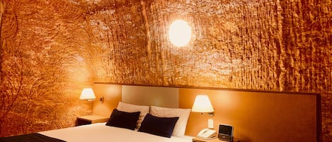 A hotel room with a textured wall, a large bed with white bedding, two bedside tables with lamps, and a nightstand with a phone.