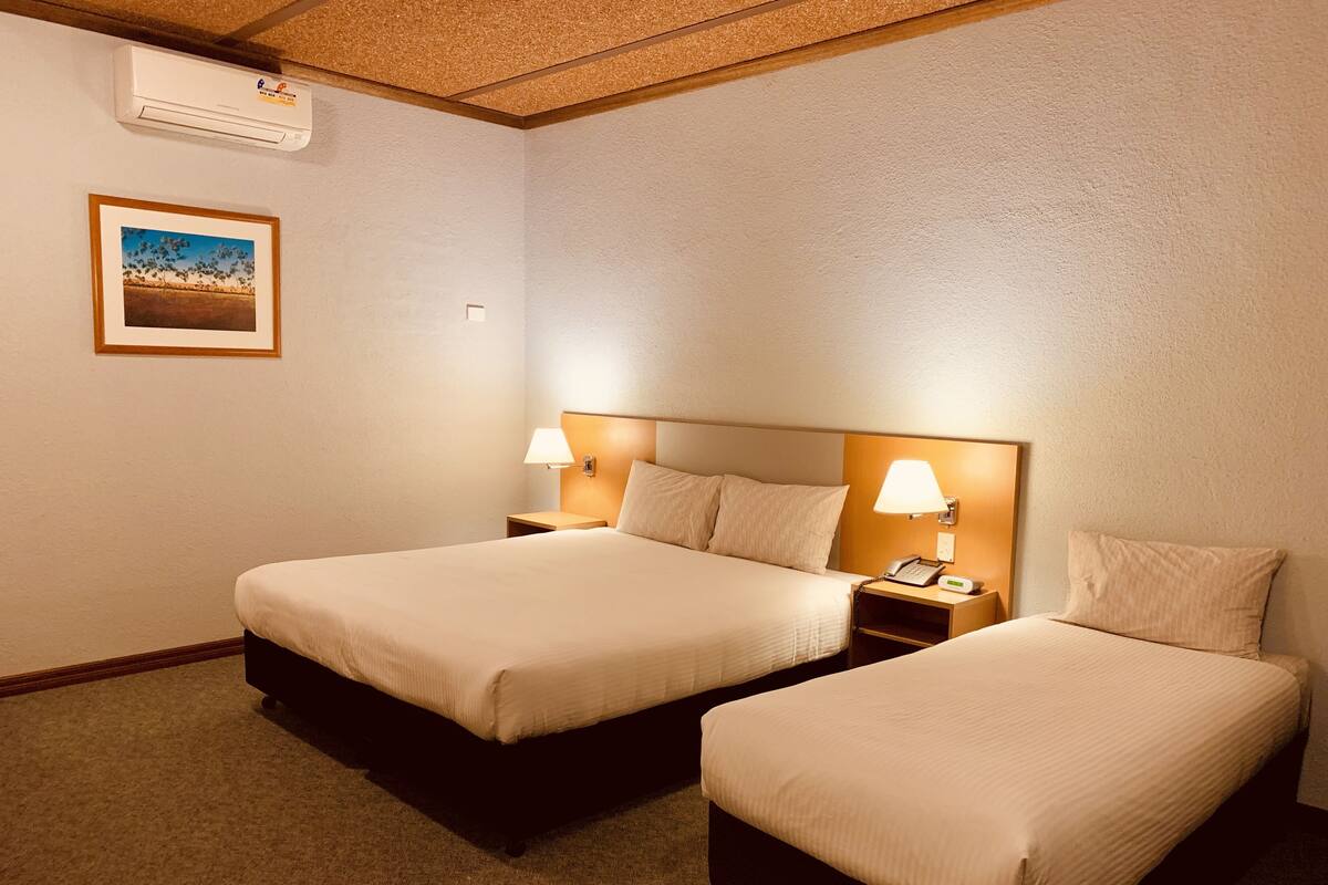 A hotel room with two beds, a nightstand with a lamp, a phone, and a picture on the wall.