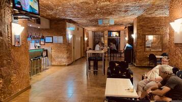 Een restaurant met een rustieke inrichting, zichtbaar aan de stenen muren en het houten plafond. Er zijn tafels en stoelen voor de gasten, en een bar met een toonbank en flessenkasten.