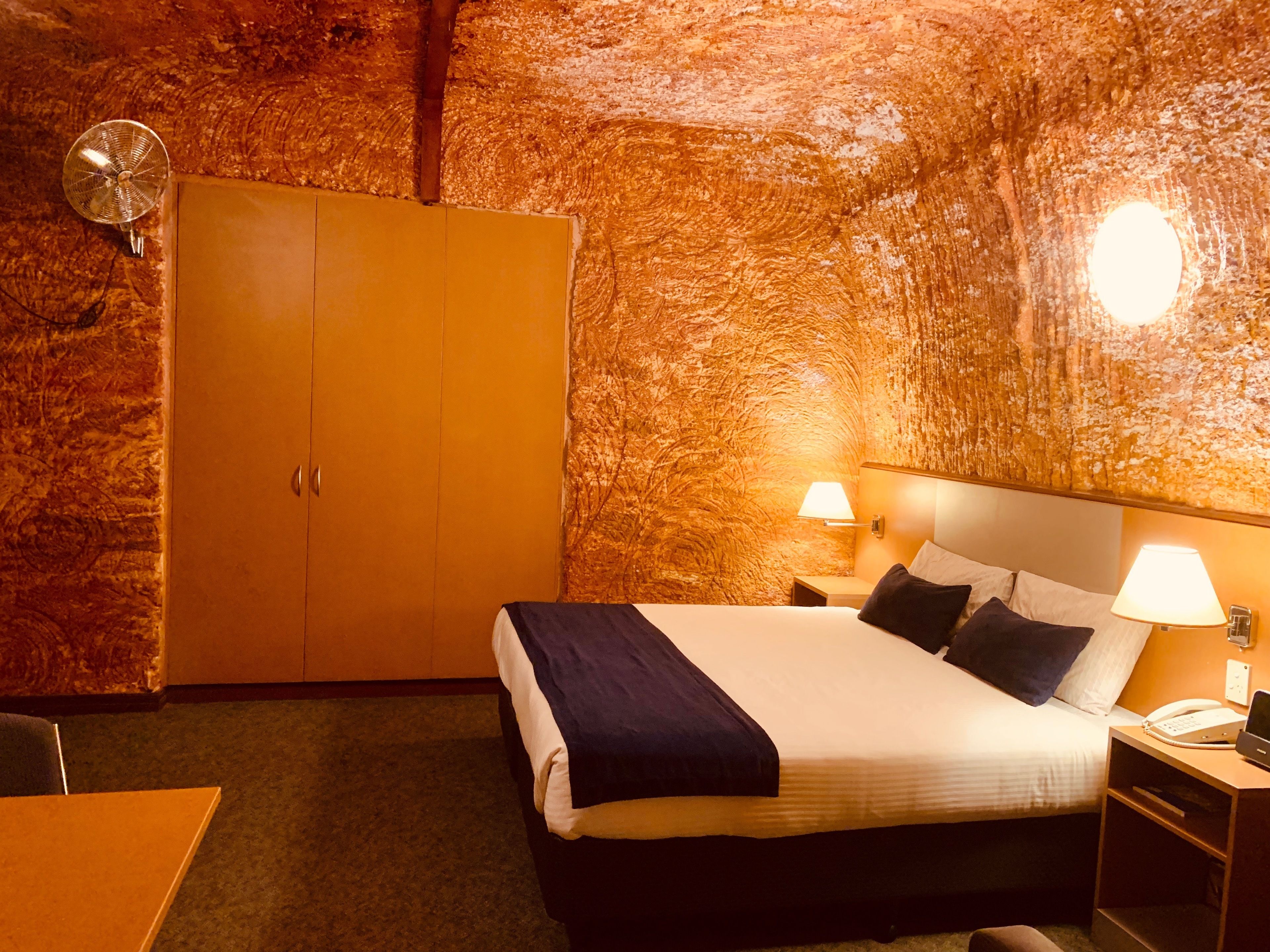 A hotel room with a bed, bedside lamps, a telephone, and a wardrobe.