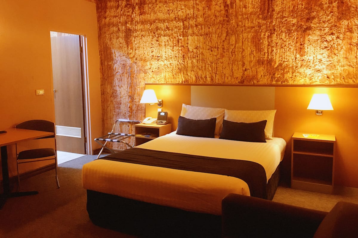 A hotel room with a large bed, bedside lamps, a desk, and a chair.