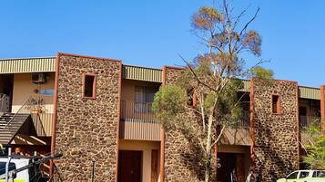 A building with stone walls and multiple balconies, a staircase, and a vehicle parked in front.
